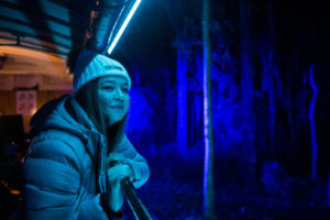 Woman travelling onboard Puffing Billy's Train of Lights. She is looking out of the open side carriage to the illuminated landscape and is wearing a warm winter coat and beanie.