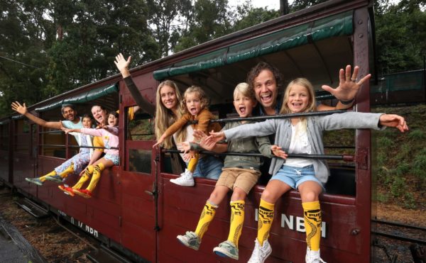 Puffing Billy riding with the legs out for kids returns to the iconic steam train attraction. Families L-R Sarah and Sagar Padwal with children Shaila 8 and Kiara 6 plus Allyssa and Jono Callow with children Adaylia 3, Asher 5 and Summer 7 celebrate the return of sitting on the carriage window sills.