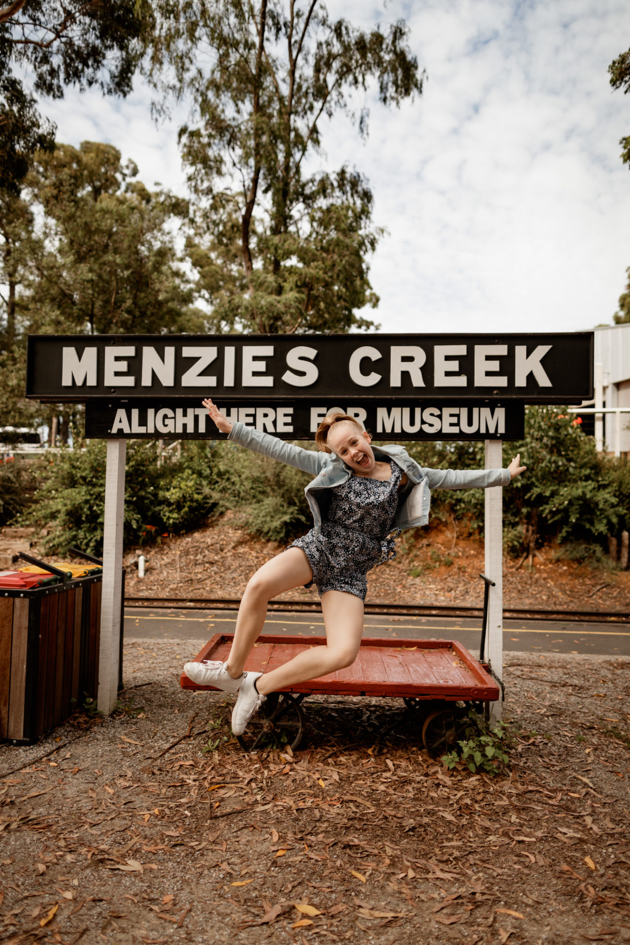 Girl Jumping Under Wooden Menzies Creek Sign