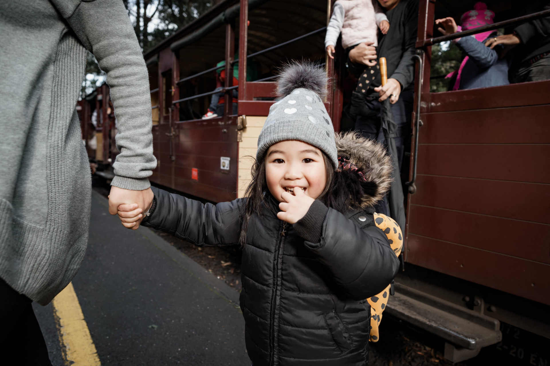 Young girl in winter clothes at Puffing Billy Railway's platform. She is holding the hand of a guardian and the train carriage can be seen in the background.