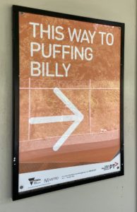 Sign at the Belgrave Metro Train station showing the way to Puffing Billy Railway. The sign has an orange background with white text saying "This way to Puffing Billy" with an arrow.