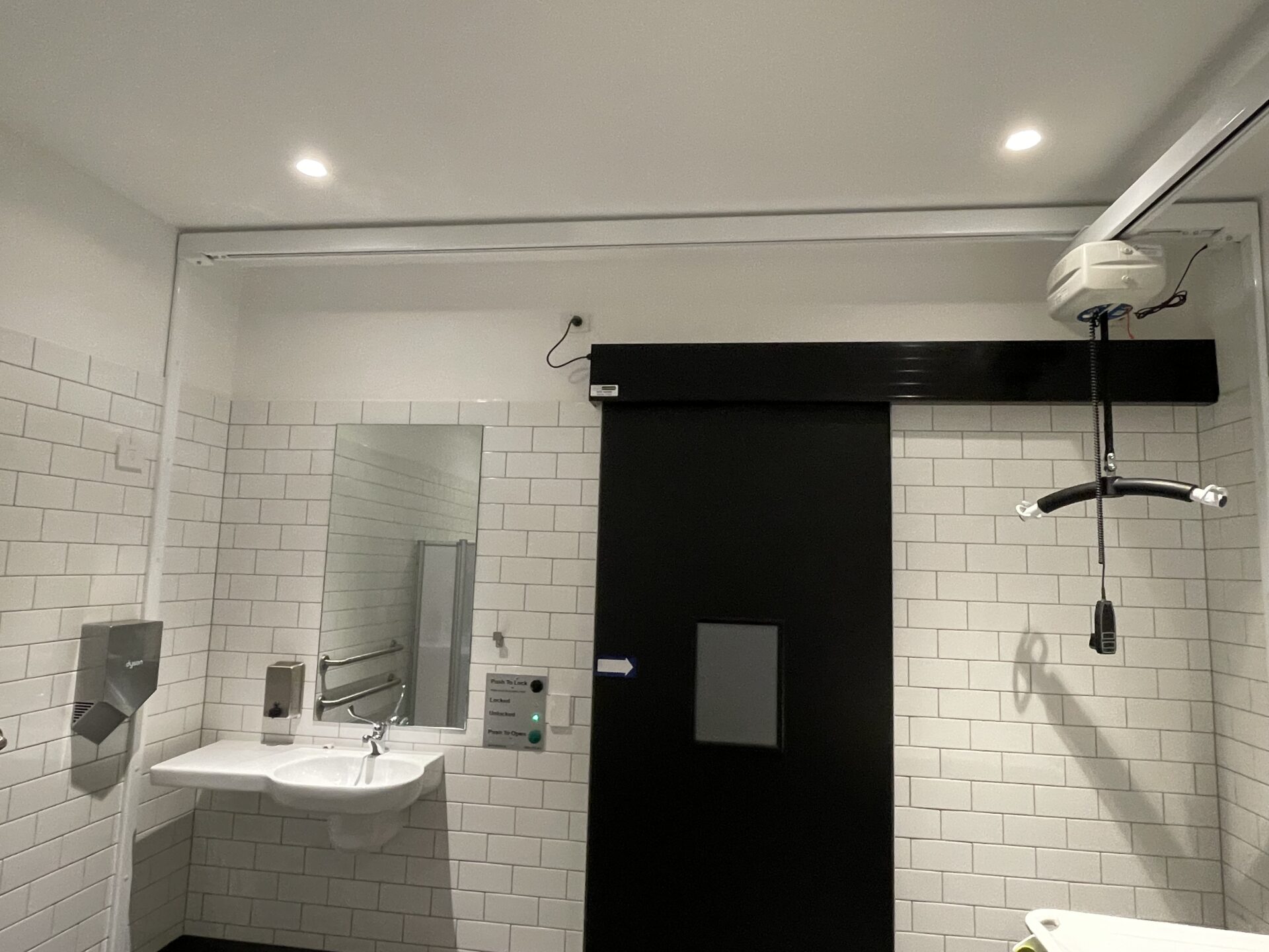 View to the doorway in the Changing Places facility, with a vanity seen on left and the adult change table and hoist seen on right.