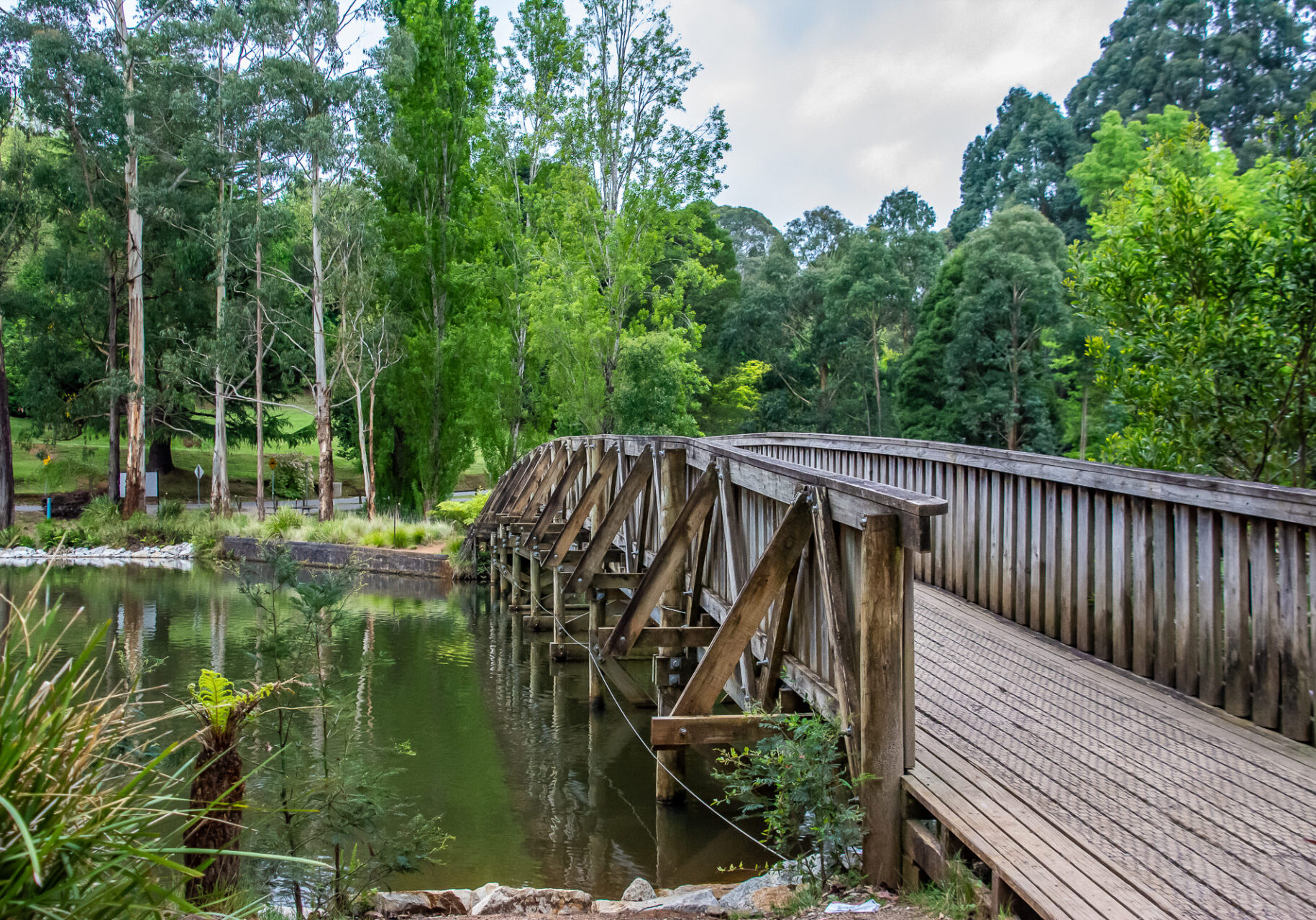 Trestle footbridge over a lake with green foliage in the background.