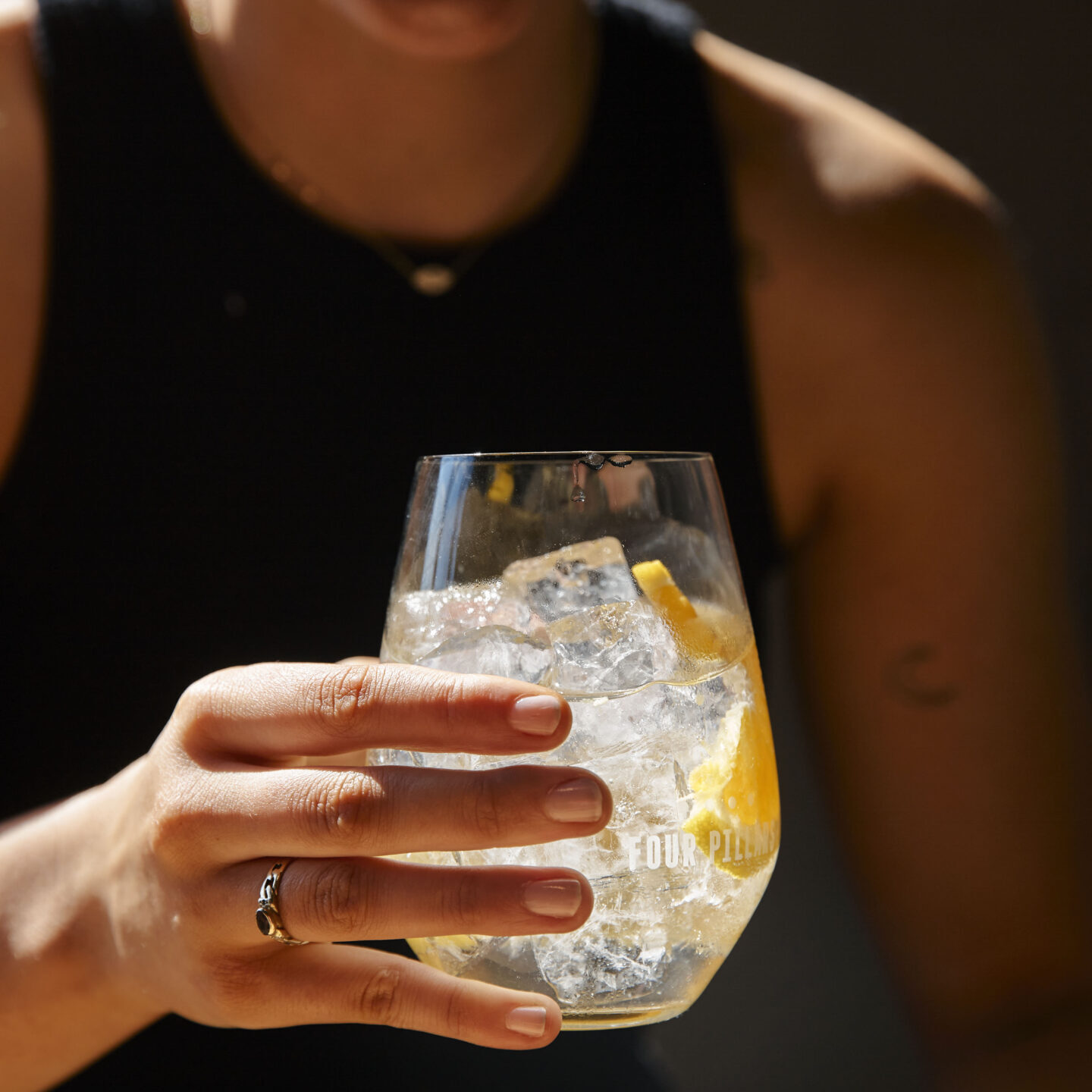 Woman in a black singlet holding a glass filled with a clear liquid and ice cubes.