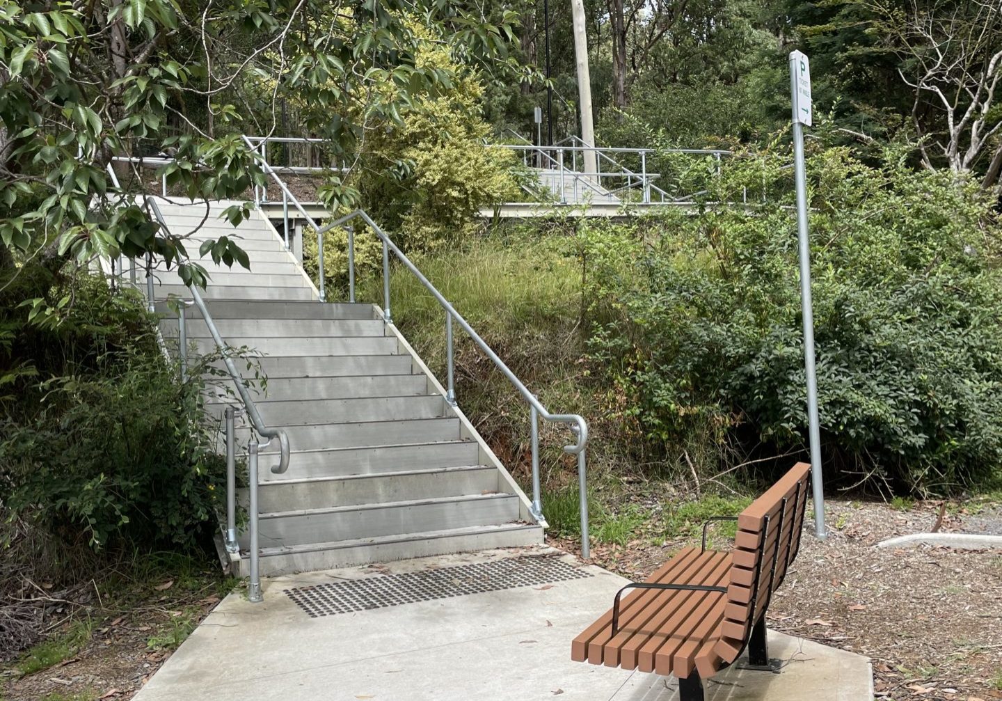 Concrete Steps From Top Lakeside Car Park. The steps has handrails and there is a wooden bench at the bottom of the steps. A concrete path continues on.