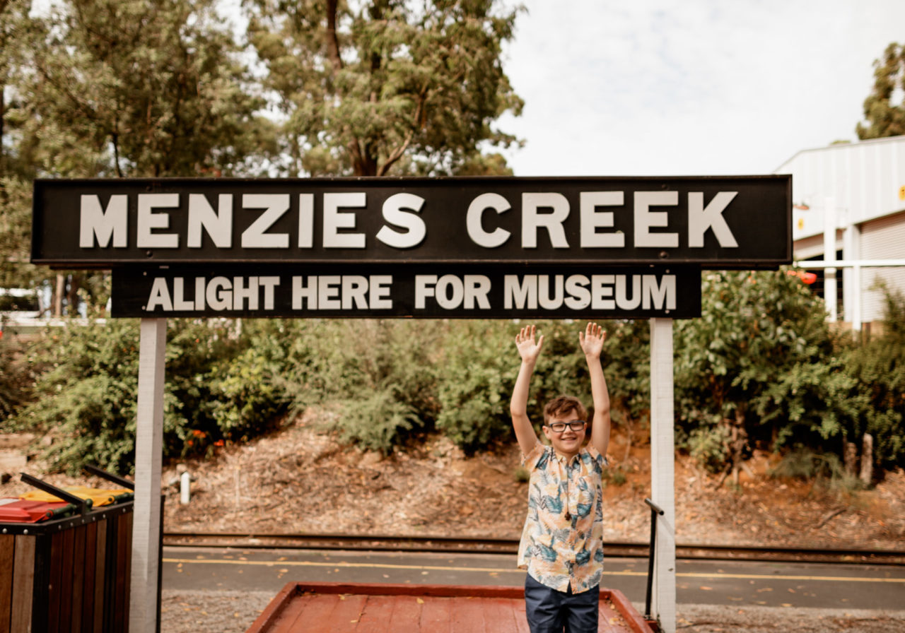 Young Boy Standing Under Menzies Creek Sign