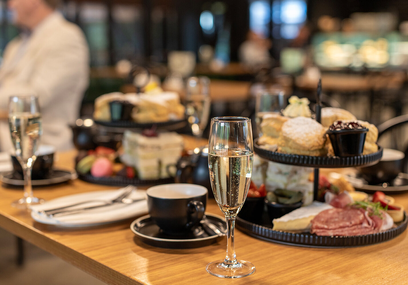 High tea served on tiered stands, with coffee and glasses of sparkling wine next to them.